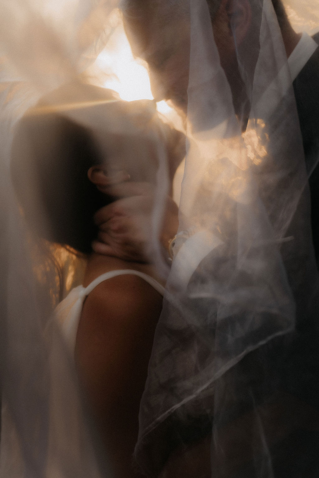 Romantisches Brautpaar unter einem Schleier bei Sonnenuntergang.