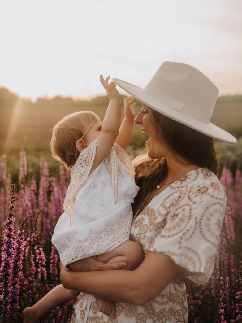 Frau mit Hut hält ein Baby auf einem Blumenfeld.